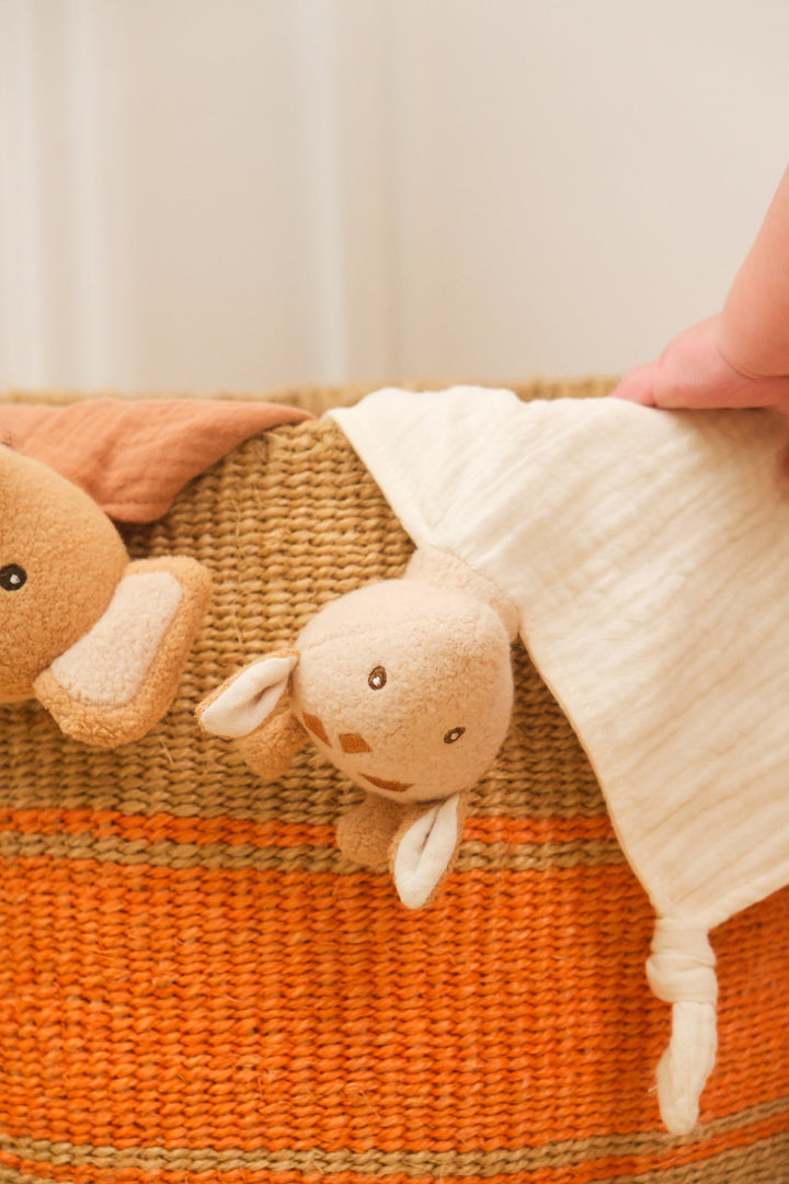Baby playing with Leonie giraffe doudou in basket