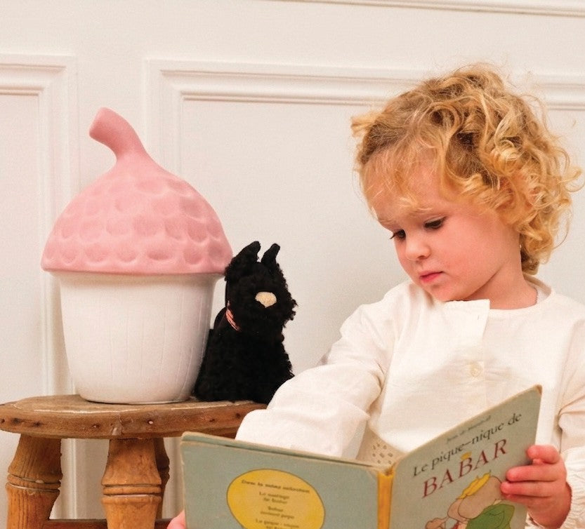 Acorn Night Lamp, Vintage Pink, on a stool beside a child reading