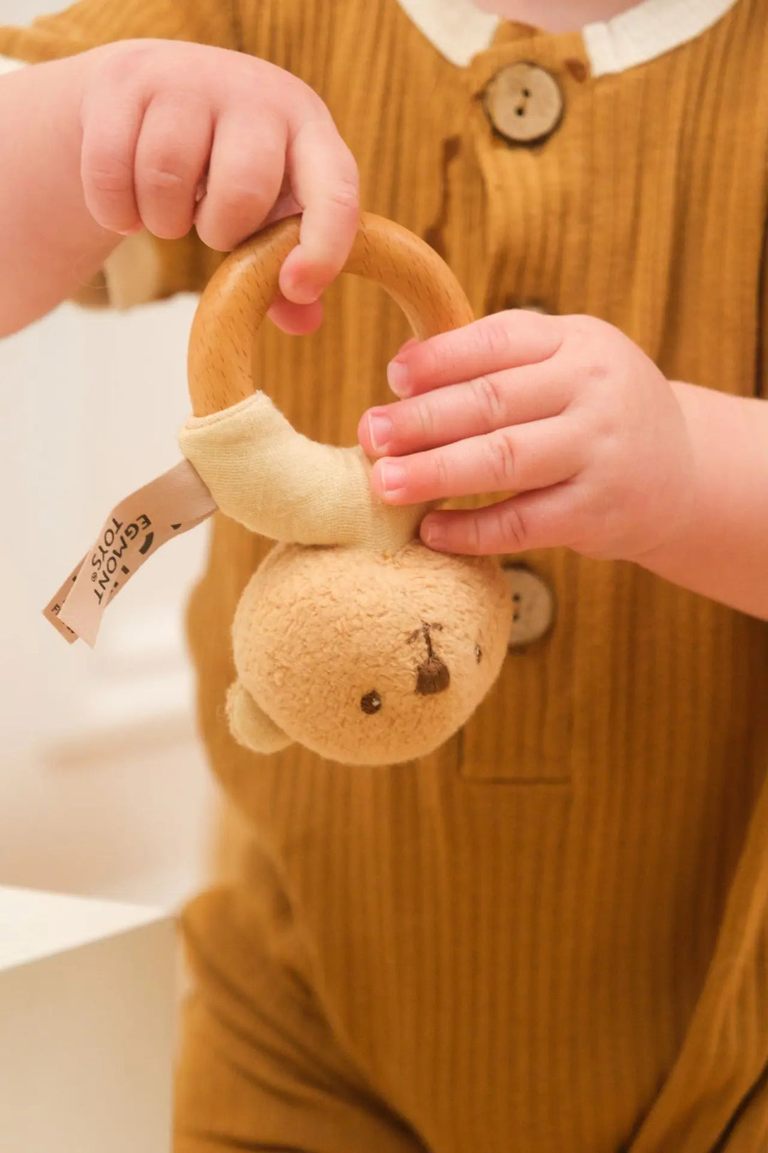Baby hands exploring Marcel bear wooden rattle (close-up)