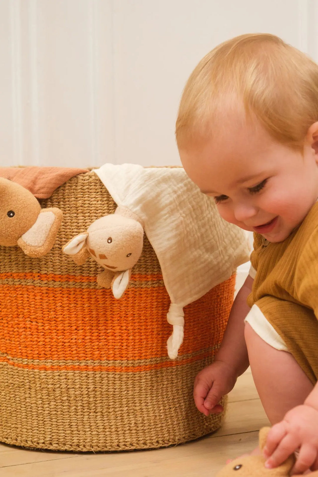Baby smiling at Leonie giraffe doudou in basket